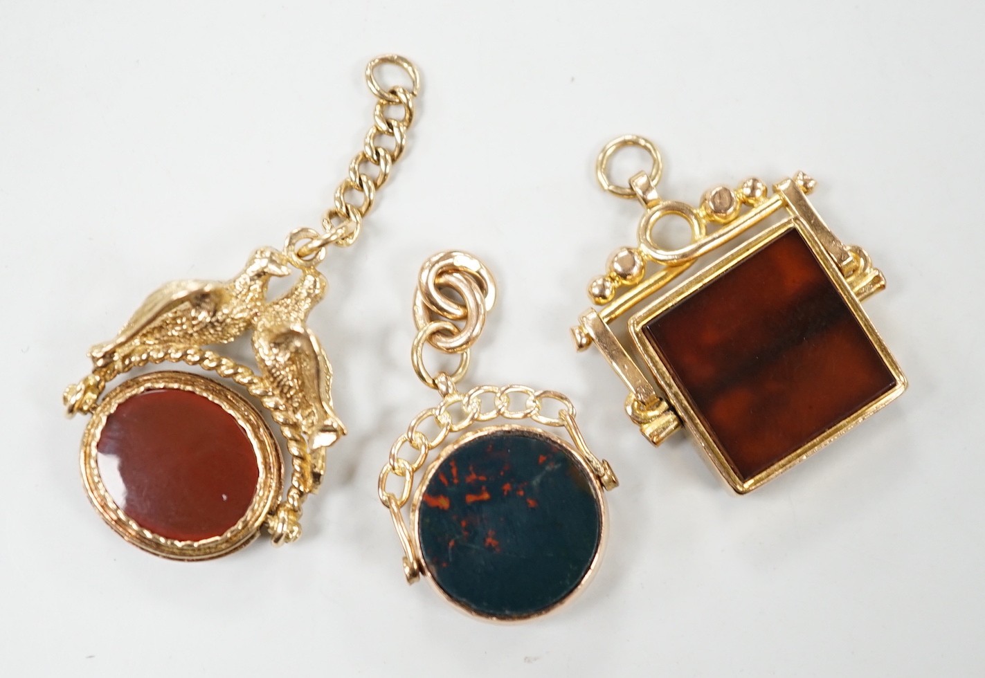 Two early 20th century 9ct gold and chalcedony set spinning fobs and one other yellow metal and chalcedony set spinning fob with twin bird finial, largest 31mm.